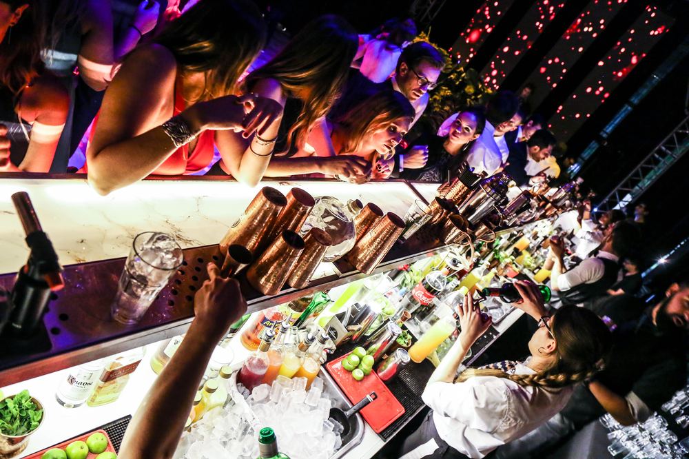 Vista aérea de invitados apoyados en la barra Holy Champagne pidiendo tragos