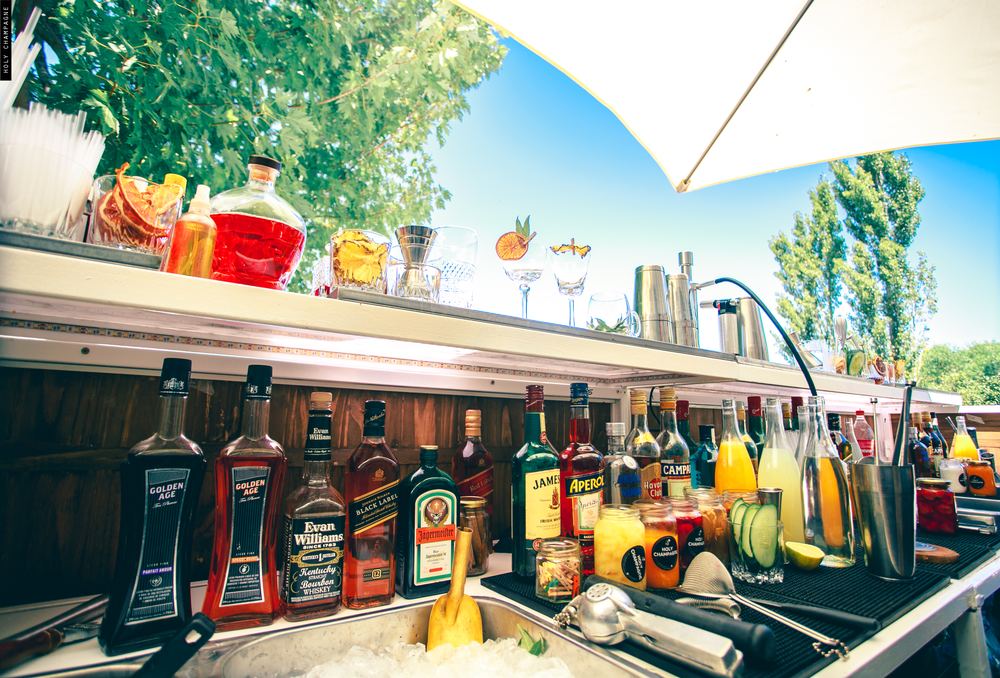 Barra móvil exterior con botellas y cítricos, montada al aire libre para un evento de día