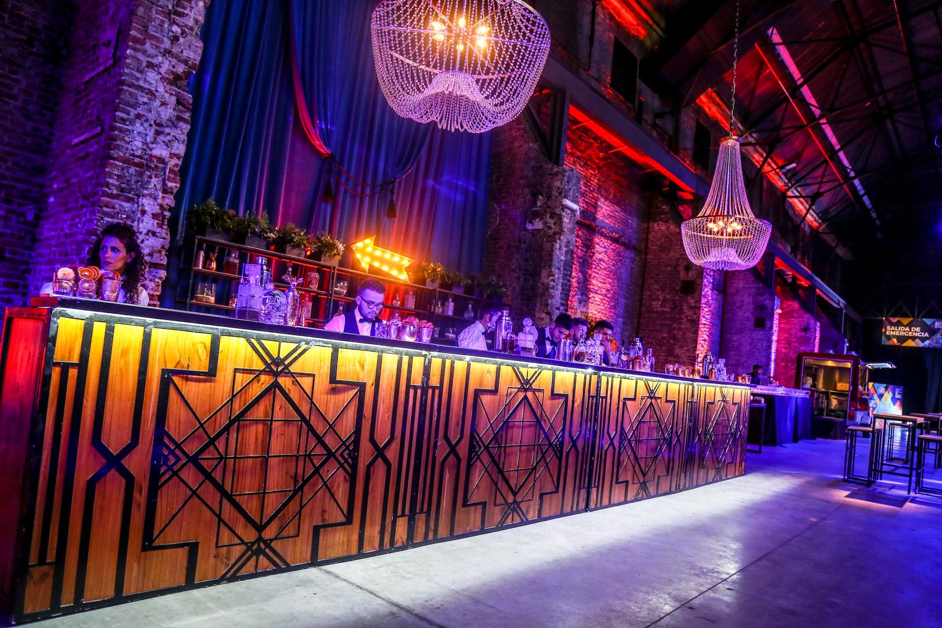 Barra de madera con diseño geométrico integrada a un salón de estilo industrial con candelabros