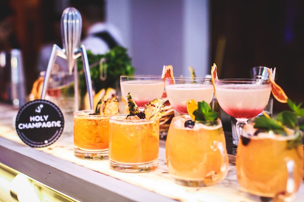 Fila de cocktails sobre la barra junto al cartel de Holy Champagne