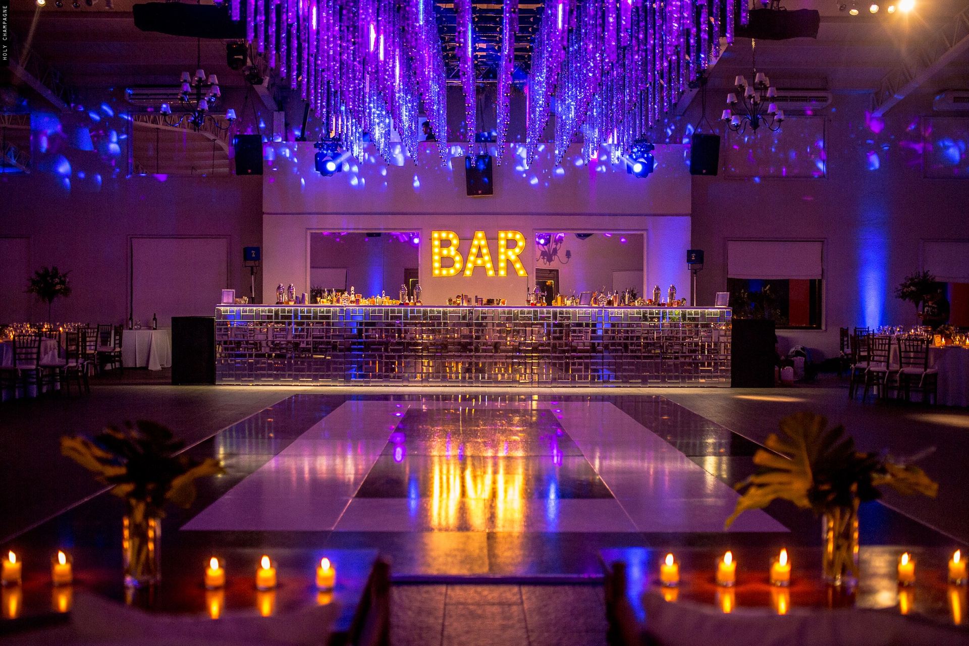 Salón de fiesta con cartel luminoso BAR, pista de baile y velas encendidas