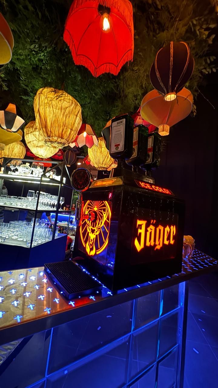 Dispensadora de shots de Jägermeister bien fríos, ambientada con faroles sobre la barra