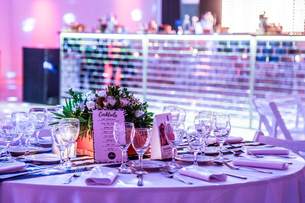 Mesa de recepción de un evento con tarjeta de cocktails y centro de flores, barra espejada de fondo