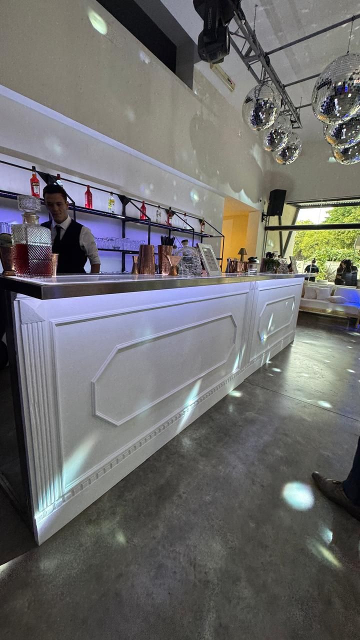 Módulo de barra blanco tallado con bartender detrás, ambientado con esferas de espejos
