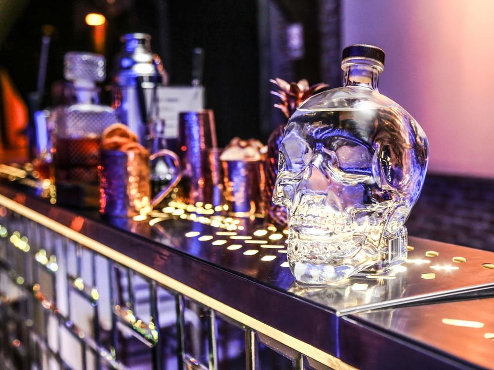Botella de vodka en forma de calavera sobre la barra espejada con luces cálidas